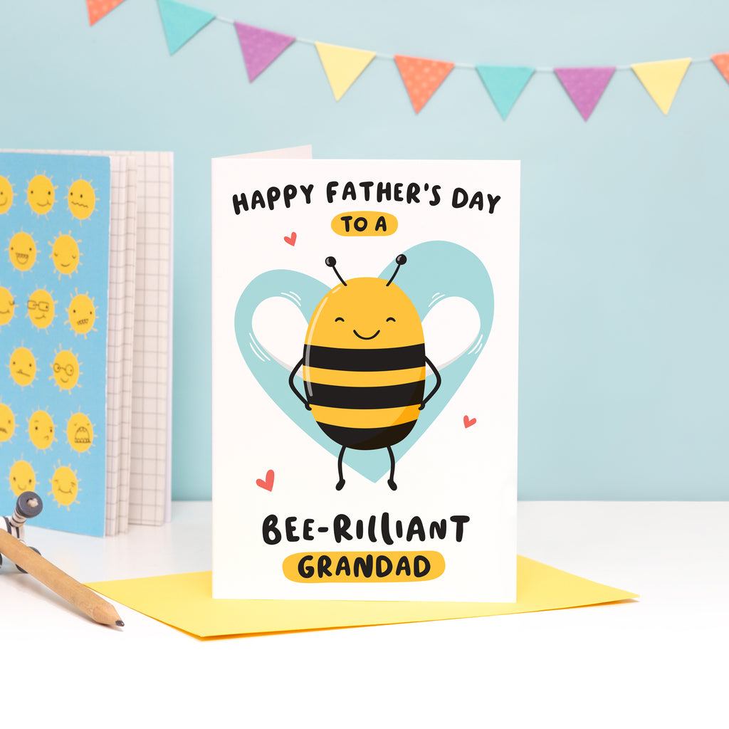 Happy Father's Day to a bee-rilliant Grandad. A cute and punny card featuring a happy bee to represent Grandad, with a light blue heart in the background.