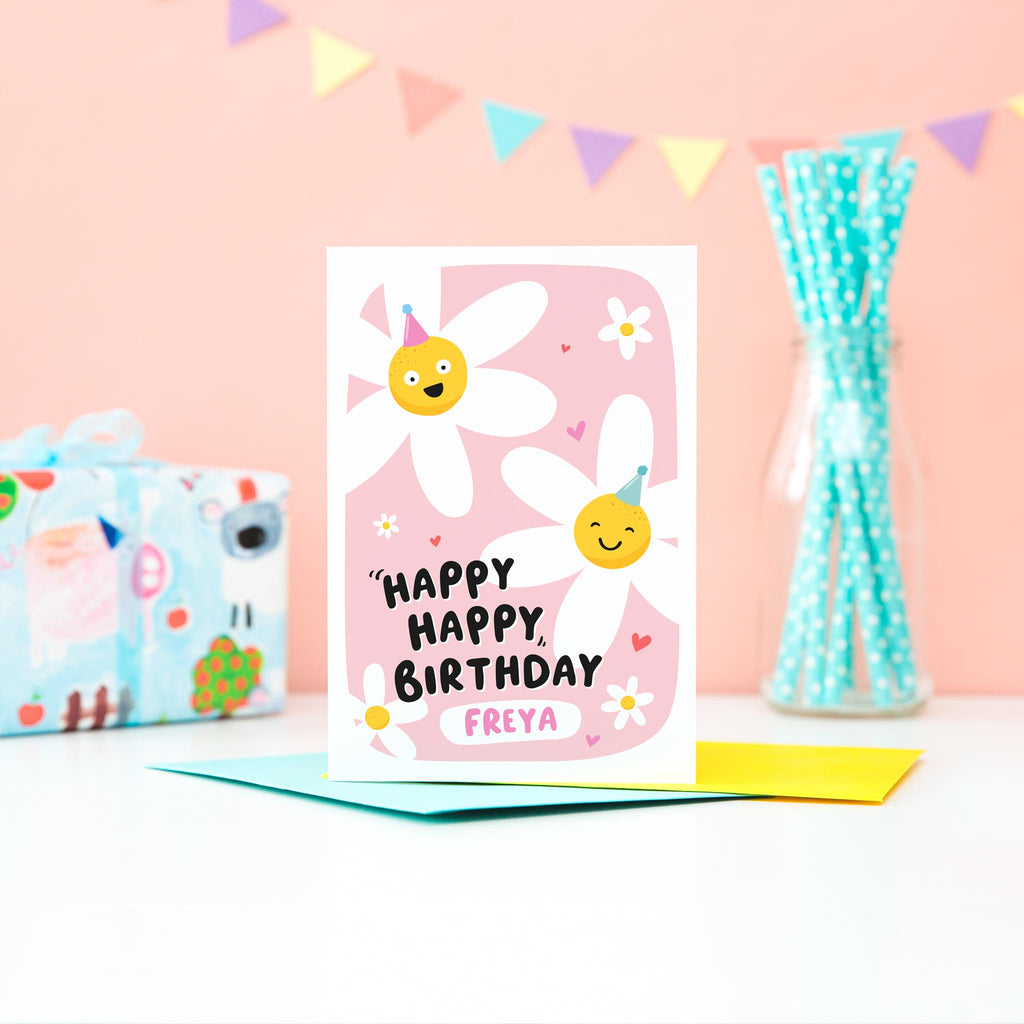 A cute card with a pink background featuring two happy daisies wearing party hats, a few hearts and the words happy happy birthday with space for personalisation underneath.