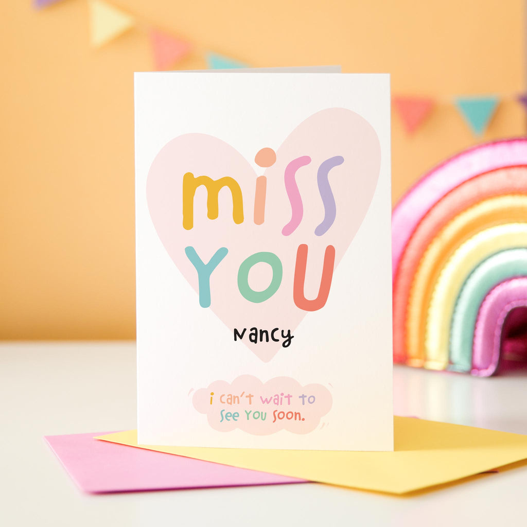 Miss you card. Cute and colourful text over a love heart. This card is personalised with the recipients name and includes the message, 'I can't wait to see you soon'