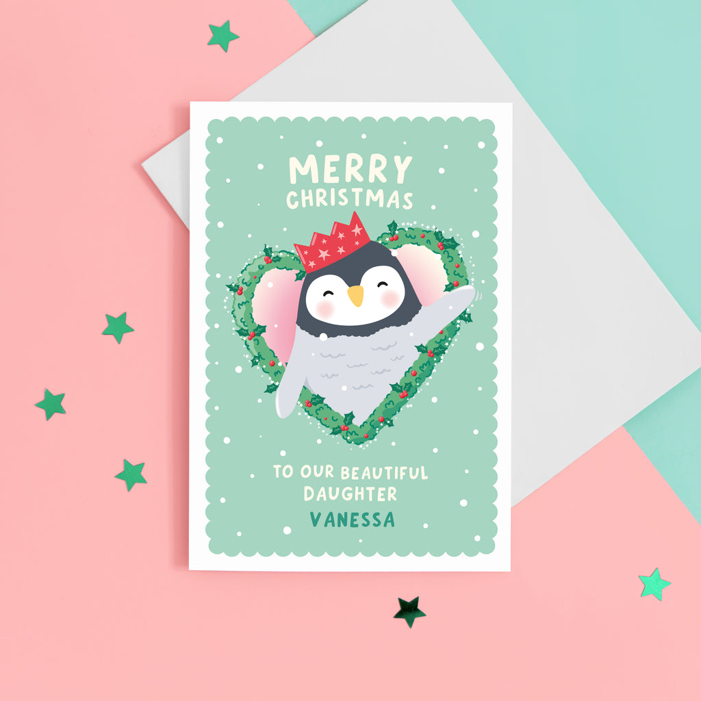 A cute Christmas card featuring a penguin popping out of a heart shaped Christmas wreath. The card reads ‘Merry Christmas to our beautiful Daughter’ with space for a name. The card can be personalised for any recipient.