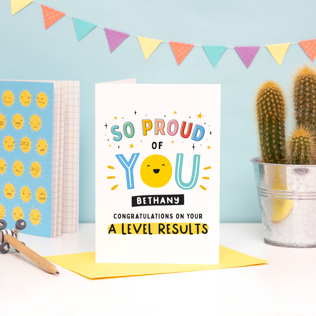 A bright and colourful A Level exam results card which reads, 'so proud of you congratulations on your A Level results. The card features a happy face on the ‘O’ of the word ‘You’ and can be personalised with a name.