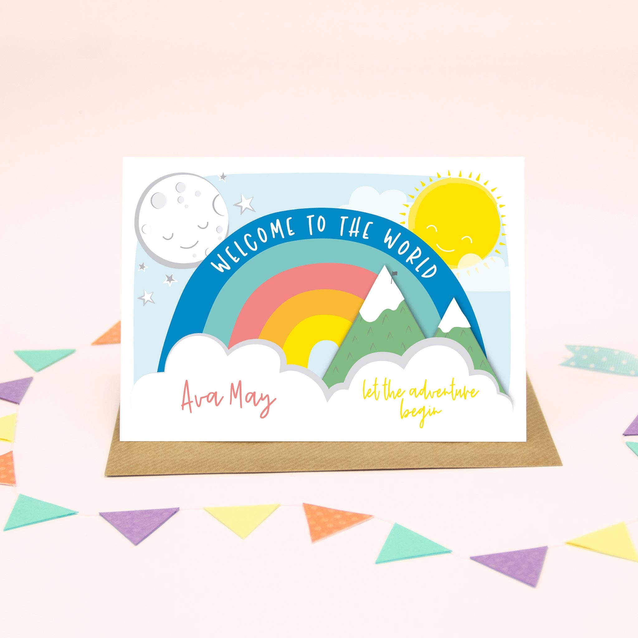 Pink writing on this colourful personalised new baby card with rainbow, sun, moon, mountains and clouds.