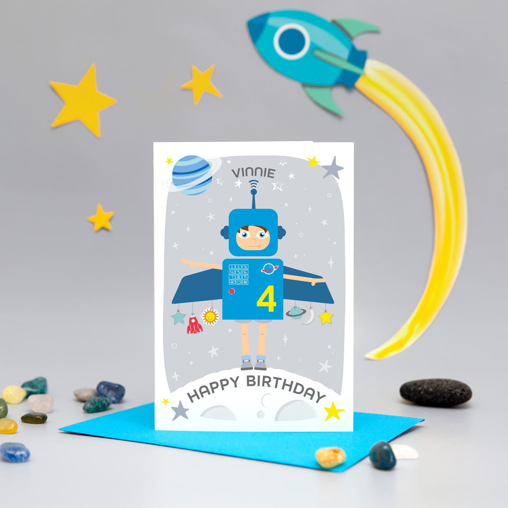 Space boy happy birthday card. This fun and colourful card shows a little boy dressed up as a blue space rocket with arms out. The card also features a moon, planets and stars. The card is personalised with any name and age.