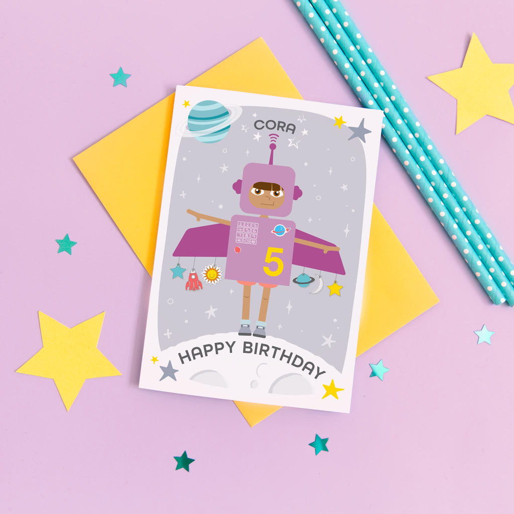 Space girl happy birthday card. This fun and colourful card shows a little girl dressed up as a purple space rocket with arms out. The card also features a moon, planets and stars. The card is personalised with any name and age.