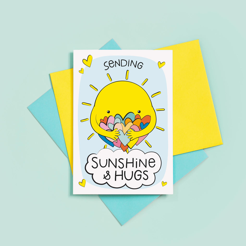 A bright and colourful cute card which features a shining sun hugging a large number of coloured love hearts. The text reads, Sending sunshine and hugs.