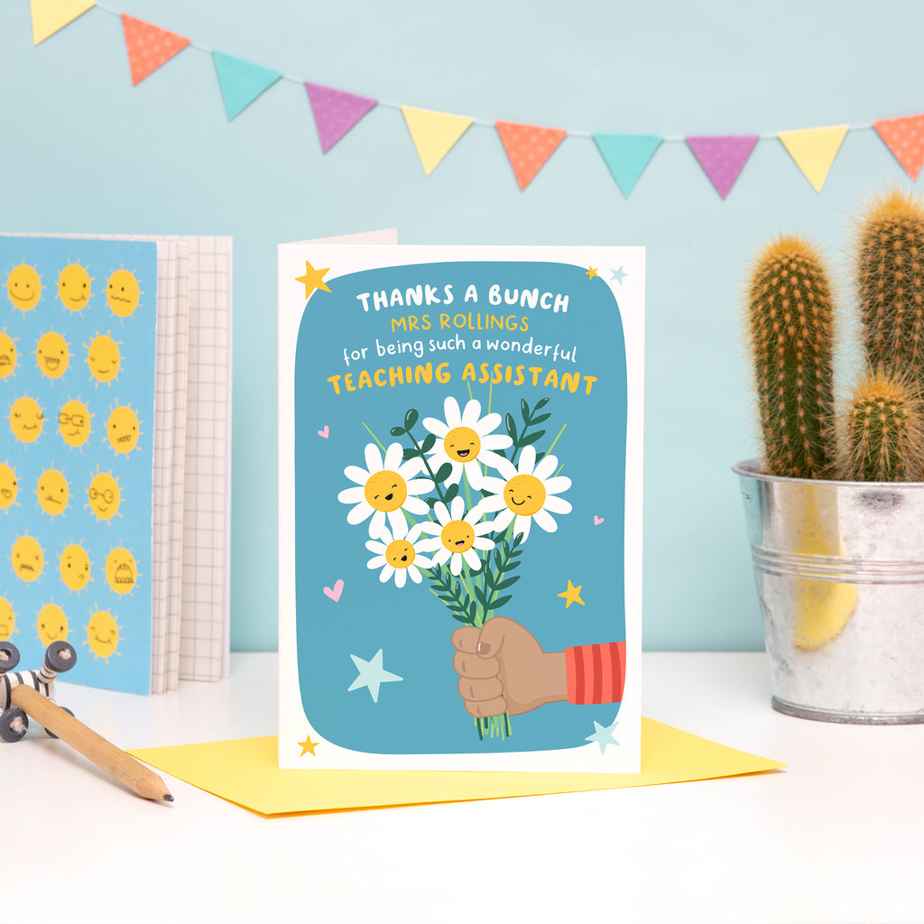 A colourful and cute card featuring a child’s hand (dark skin) holding a bunch of happy flowers. The card reads ‘thanks a bunch (teachers name) for being such a wonderful teaching assistant’.