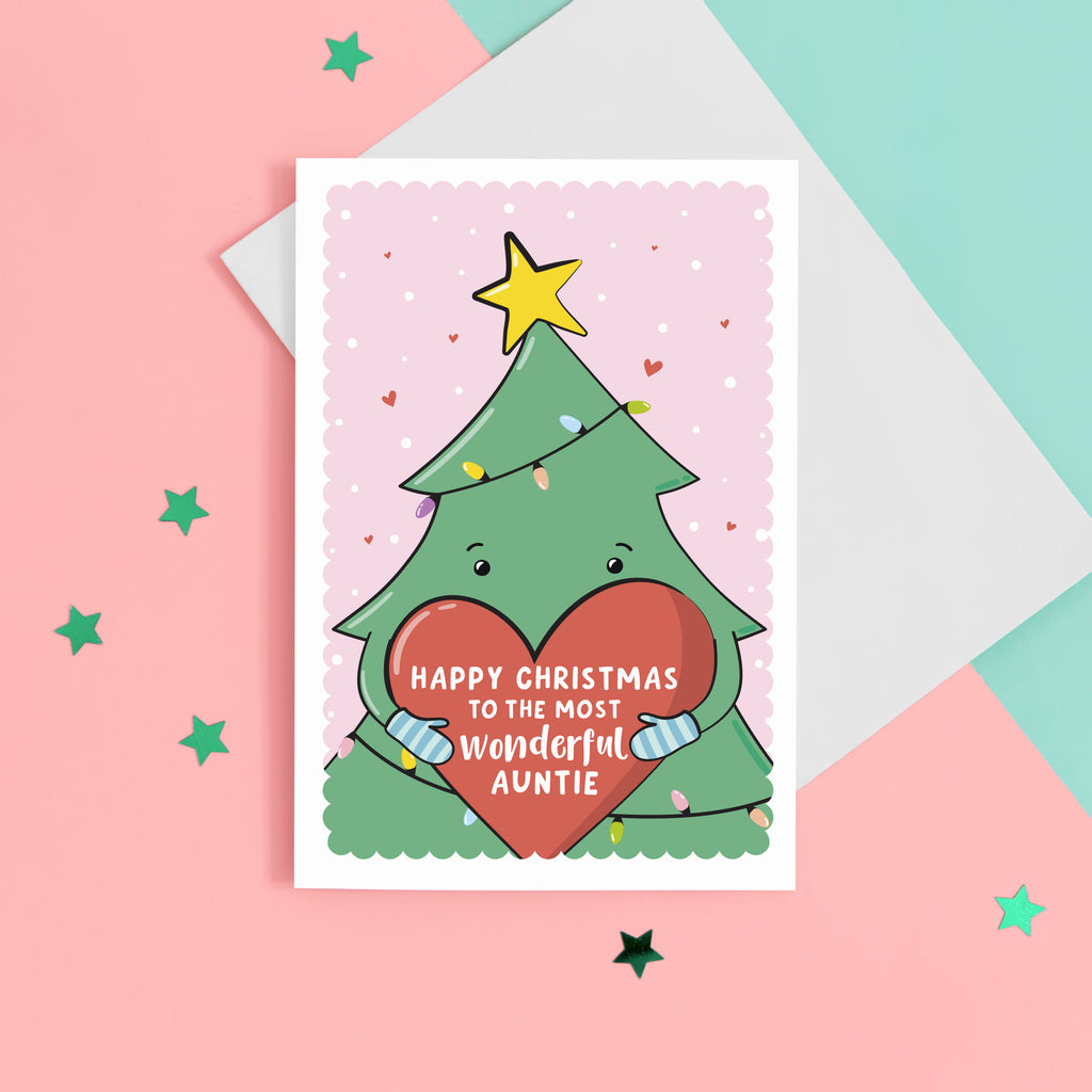 A cute Christmas card featuring a cartoon Christmas tree hugging a large love heart. The love heart reads, "Happy Christmas to the most wonderful Auntie". A yellow star is on the top of the tree set against a light pink snowy background with love hearts.