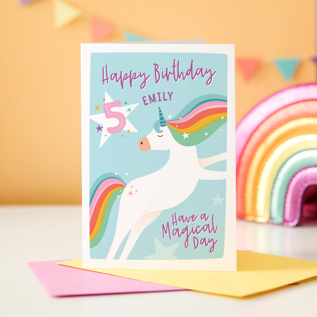 A bright and colourful girls birthday card featuring a unicorn with a rainbow tail and mane. The card can be personalised with a name and and age. The photo example reads 'Happy Birthday Emily have a magical day' and details age 5.