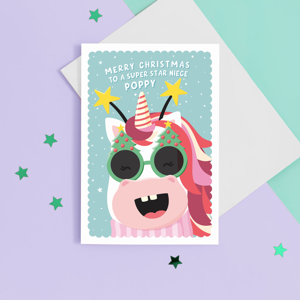 A fun and colourful Christmas card featuring a happy unicorn face, wearing festive Christmas glasses and a star headband. The card reads ‘Merry Christmas to a super star Niece’ but can be personalised for any recipient and has space to add the recipients name.