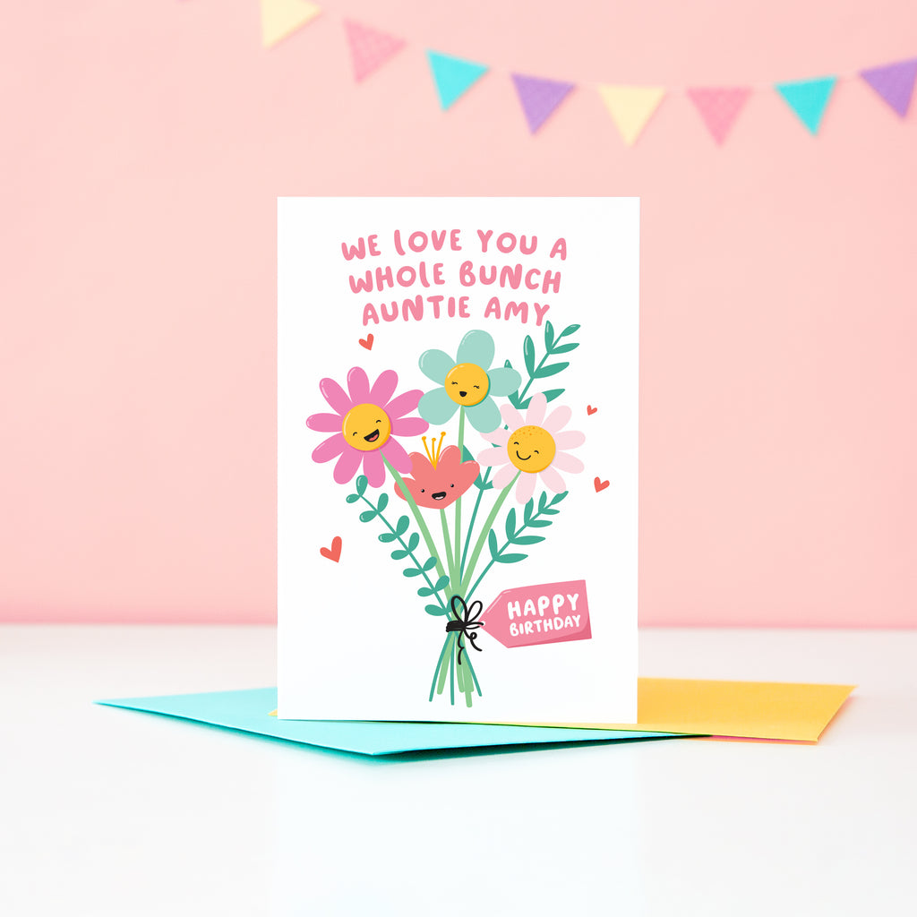 A super cute birthday card for an Auntie, featuring a bunch of happy smiling flowers and a collection of small hearts. The card reads, ‘we love you a whole bunch’ with space to personalise with Auntie’s name. 