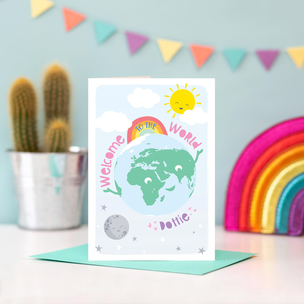 Greetings card with smiling earth character plus sun, moon and rainbow. text says welcome to the world and includes any personalised name in purple