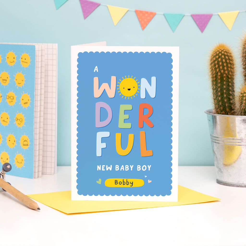 A colourful card featuring the words 'a wonderful new baby boy' with space to personalise with a name. The card has a blue background and the word 'wonderful' has bright colours with a smiley sunshine face for the letter 'o'.