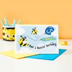 Load image into Gallery viewer, Cute personalised bee birthday card shows two bees in the sky with clouds pulling balloons with any name and age added. Shown here with blue balloons.
