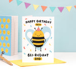 Load image into Gallery viewer, Happy birthday to a bee-rilliant Dad. A cute and punny card featuring a happy bee wearing a party hat to represent Dad, with a light blue heart in the background and a sprinkle of confetti.
