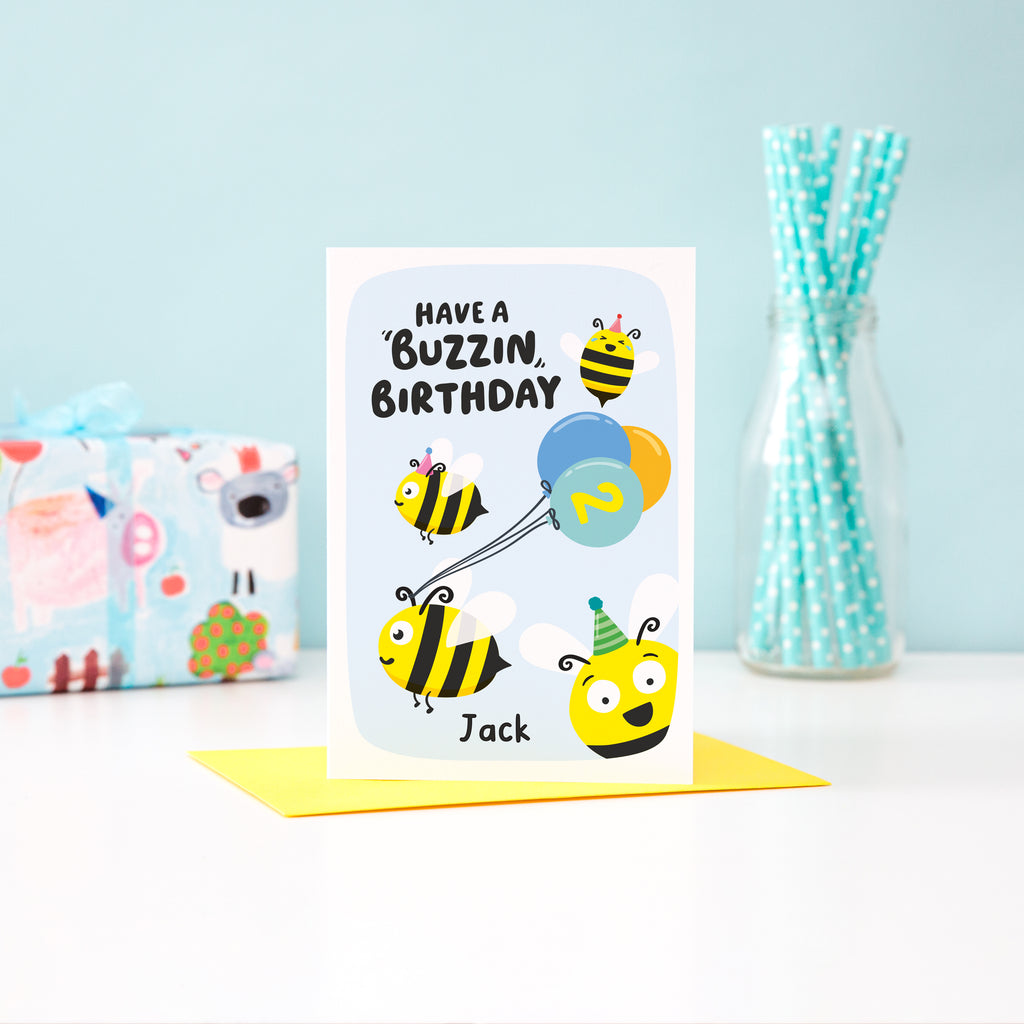 Cute personalised bee birthday card shows four bees in the sky with one pulling a bunch of  balloons. Any name and age added.