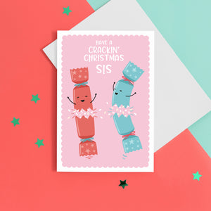 A funny Christmas card with a pink background, featuring two happy Christmas crackers and the words 'have a crackin' Christmas Sis'.