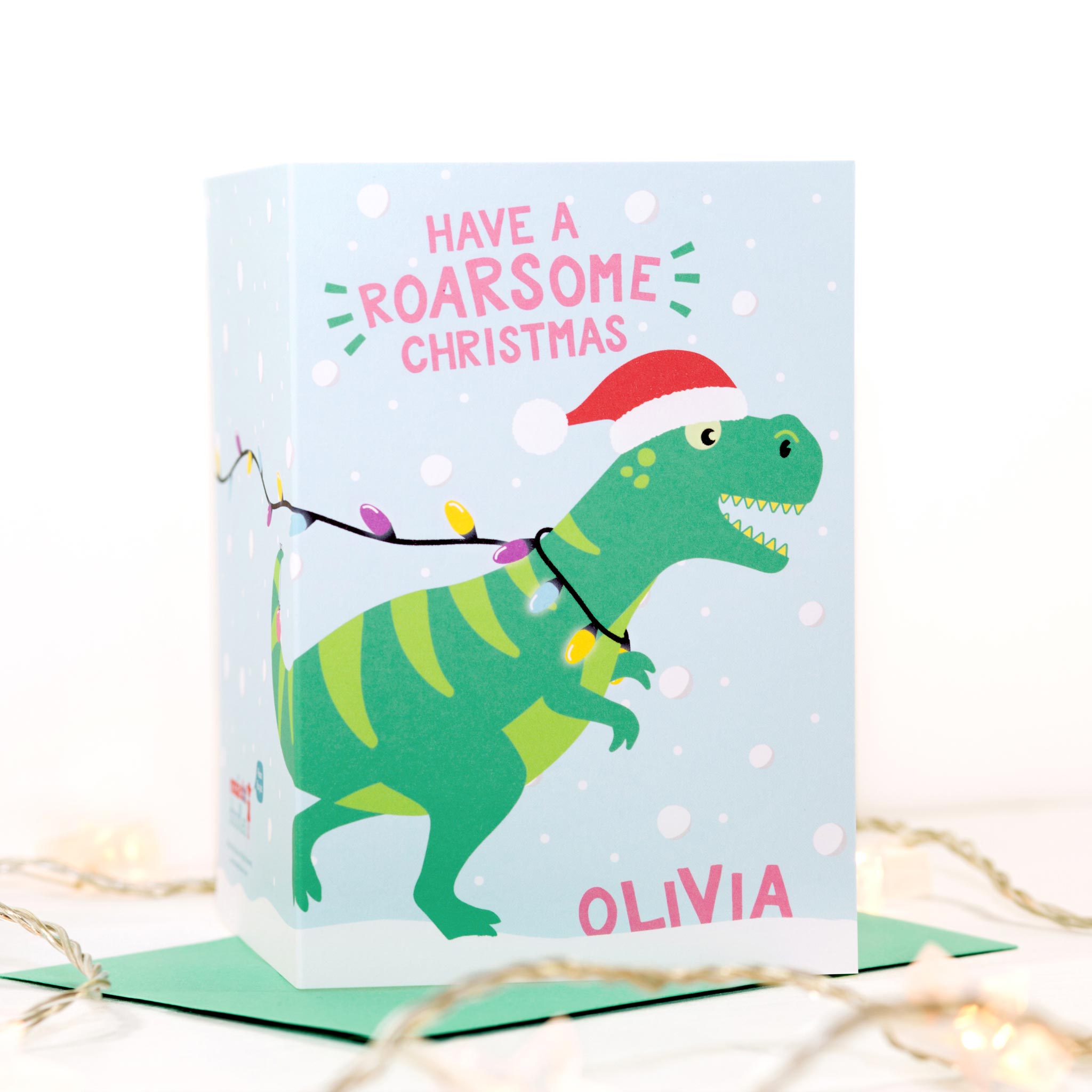 Have a roarsome Christmas. A fun Christmas card featuring a T-rex running accross the card tangle in Christmas lights. This version features pink text and includes any name personalisation.