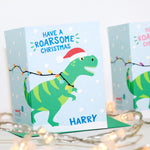 Load image into Gallery viewer, Have a roarsome Christmas. A fun Christmas card featuring a T-rex running accross the card tangle in Christmas lights. This version features blue text and includes any name personalisation.
