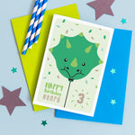 Load image into Gallery viewer, Happy birthday card with cute baby Triceratops face on a balloon and any personalised name and age.
