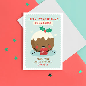 A super cute card featuring a happy little Christmas pudding illustration, holding a present. The card reads 'Happy 1st Christmas as my Daddy from your little pudding', with space to personalise with the baby's name.