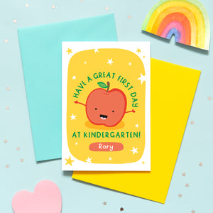 This card has a bright yellow background with white stars, and features a smiling happy apple with outstretched arms, and the words, 'Have a great first day at kindergarten'. There is a space underneath the text to personalise the card with the reciepients name.