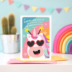 A fun and colourful birthday card featuring a happy unicorn face, wearing heart glasses and a star headband. The card reads ‘Happy Birthday to a super star Granddaughter’ but can be personalised for any recipient and has space to add the recipients name.