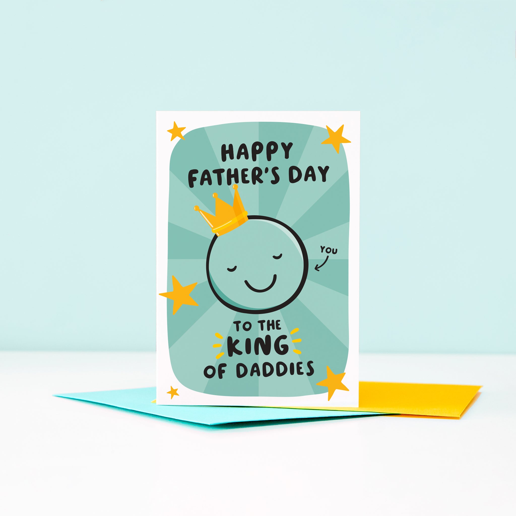 A bold and colourful card featuring a smiling face wearing a crown and the words Happy Father's Day to the King of Daddies. The card has a sea green starburst background with bright yellow stars.