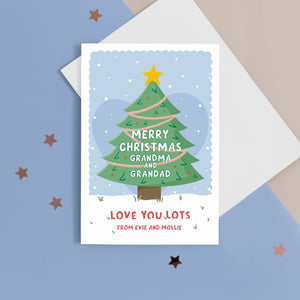 Merry Christmas Grandma & Grandad. Love you lots. A beautiful Christmas card with a festive tree, star and love hearts on a snowy background in blue. The card can be name customised for the grandparents and can include who the card is from at the bottom.