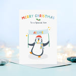 Load image into Gallery viewer, A cute and colourful Christmas card featuring a penguin holding a banner which can be personalised with a child’s name. The card reads Merry Christmas to a Special Son – the card can be customised for any recipient.
