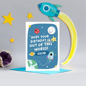 A cute and colourful card with a space theme, featuring happy planets, stars and a rocket with a blue background. The wording on the card says hope your birthday is out of this world with a space for personalising with a name.