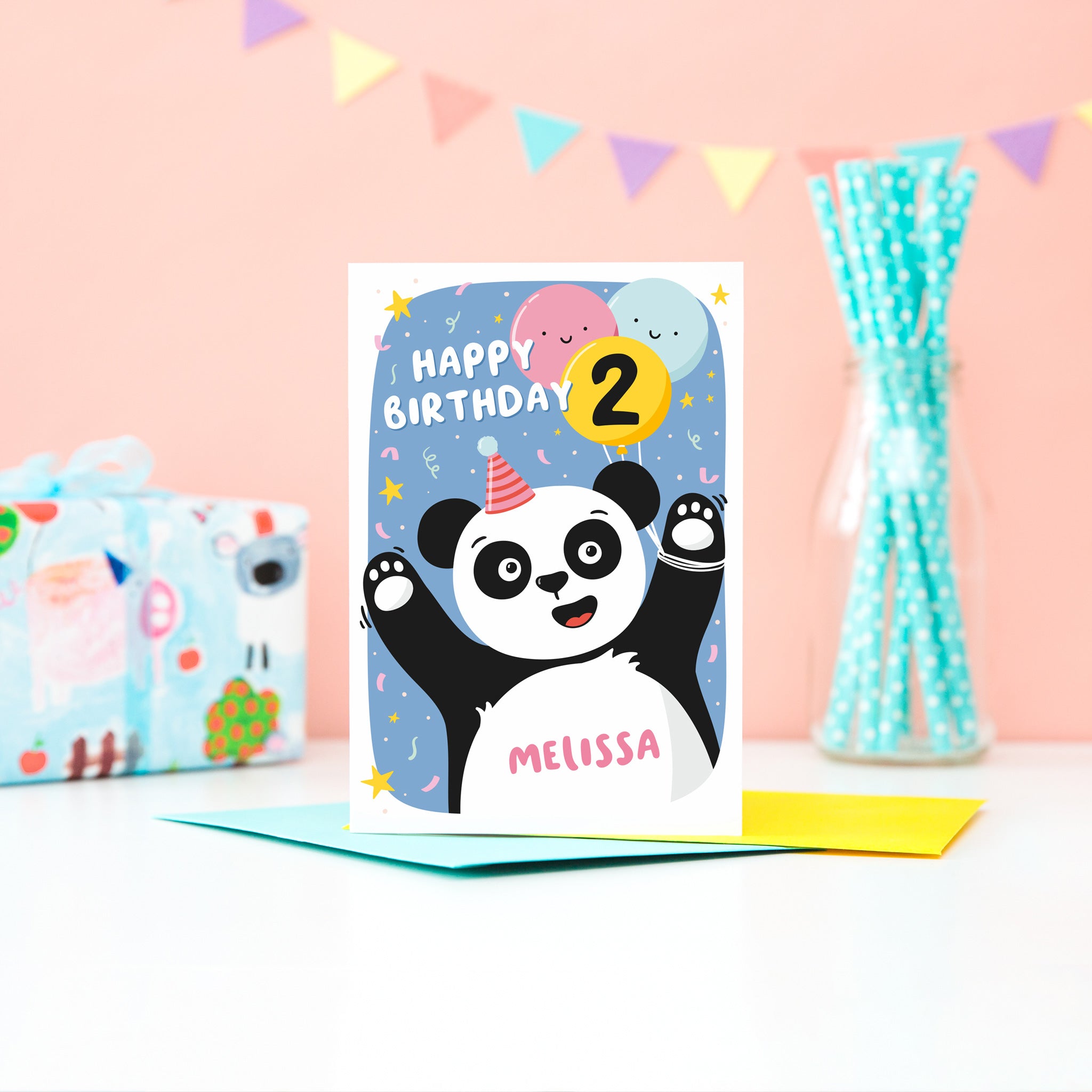 A fun and colourful card featuring a happy panda wearing a party hat, a collection of smiling balloons and a pop of confetti. There is space on a balloon to detail the childs age and there is space to personalise the card with a name on the pandas tummy.