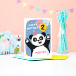 Load image into Gallery viewer, A fun and colourful card featuring a happy panda wearing a party hat, a collection of smiling balloons and a pop of confetti. There is space on a balloon to detail the childs age and there is space to personalise the card with a name on the pandas tummy.
