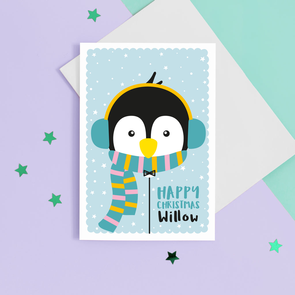 Happy Christmas. A cute personalised christmas card featuring a penguin in snow wrapped up with earmuffs and scarf. Add any name to this Christmas card.