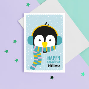 Happy Christmas. A cute personalised christmas card featuring a penguin in snow wrapped up with earmuffs and scarf. Add any name to this Christmas card.