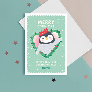 A cute Christmas card featuring a penguin popping out of a heart shaped Christmas wreath. The card reads ‘Merry Christmas to our beautiful Granddaughter’ with space for a name. The card can be personalised for any recipient.