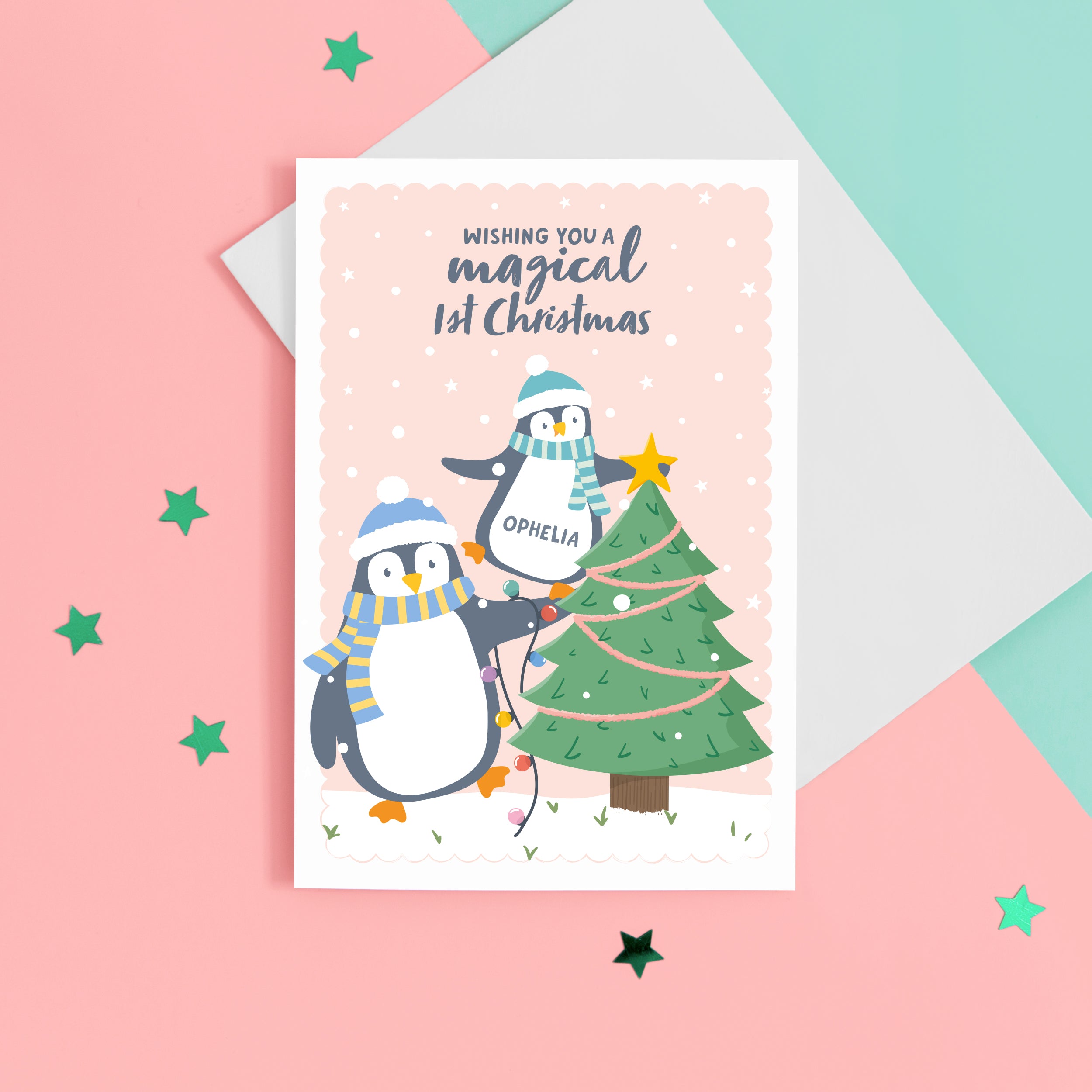 A cute Christmas card with a light peach background, featuring a baby penguin balancing on a big penguin whilst putting a star on the top of a Christmas tree. The card reads ‘Wishing you a magical 1st Christmas’. The card has space to place the baby’s name on the baby penguins belly.