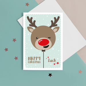 Happy Christmas. A cute personalised christmas card featuring a cheeky red nosed reindeer in snow and stars. Add any name to this Christmas card.