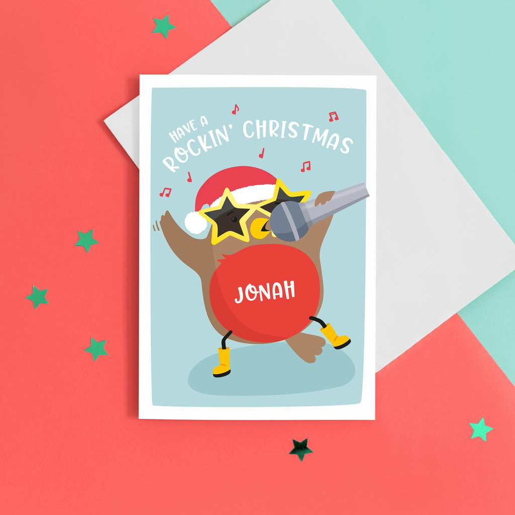 A colourful and happy card featuring a dancing and singing robin, wearing a santas hat, big star glasses and wellies. The card reads 'have a rockin' Christmas' with space to personalise with a name.