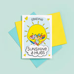 Load image into Gallery viewer, A bright and colourful cute card which features a shining sun hugging a large number of coloured love hearts. The text reads, Sending sunshine and hugs.
