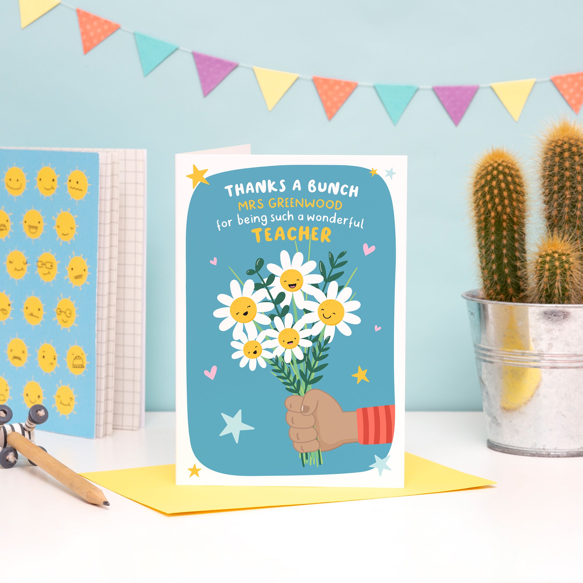 A colourful and cute card featuring a child’s hand (dark skin) holding a bunch of happy flowers. The card reads ‘thanks a bunch (teachers name) for being such a wonderful teacher’.