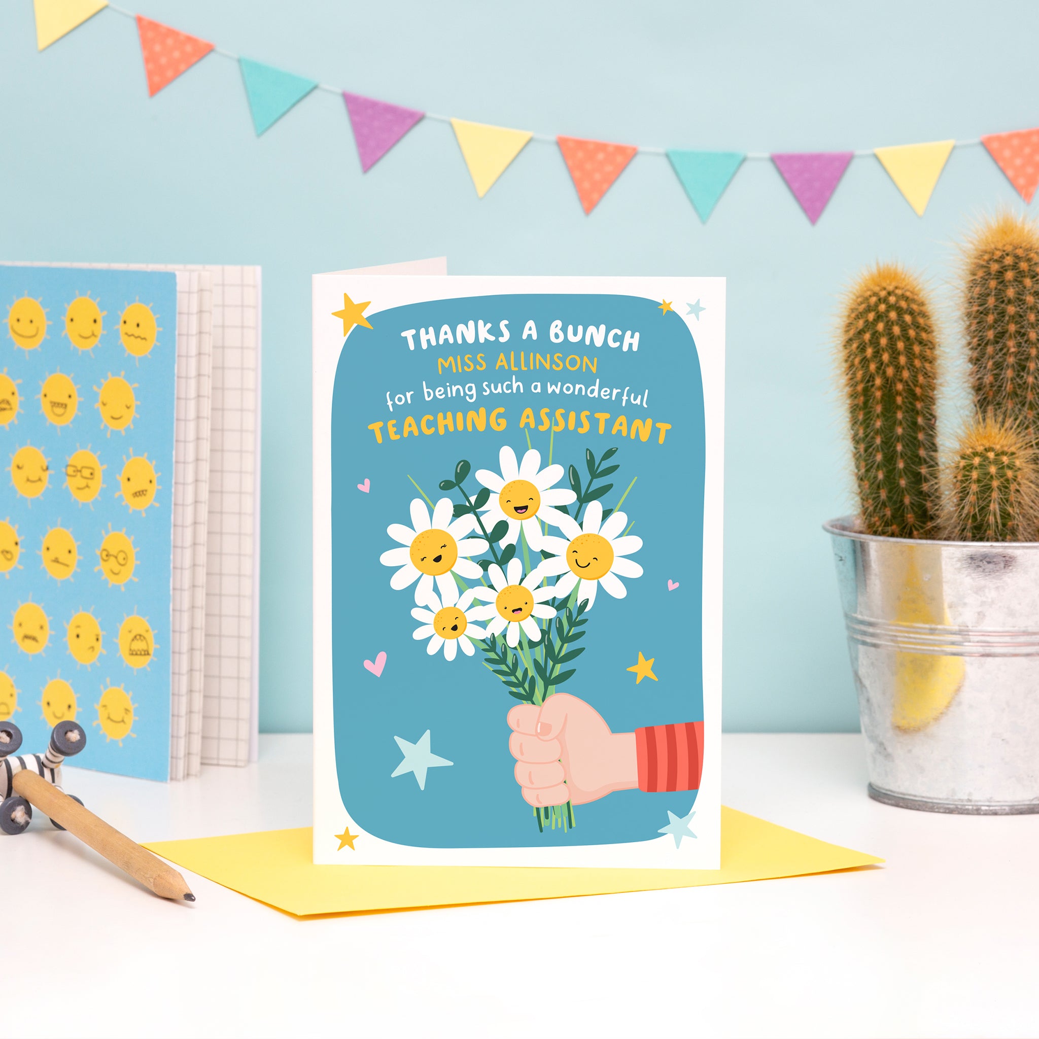 A colourful and cute card featuring a child’s hand (fair skin) holding a bunch of happy flowers. The card reads ‘thanks a bunch (teachers name) for being such a wonderful teaching assistant’.