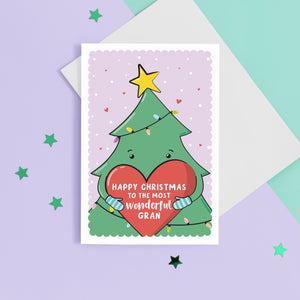 A cute Christmas card featuring a cartoon Christmas tree hugging a large love heart. The love heart reads, "Happy Christmas to the most wonderful Gran". A yellow star is on the top of the tree set against a light purple snowy background with love hearts.