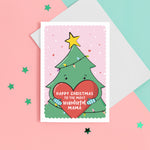 Load image into Gallery viewer, A cute Christmas card featuring a cartoon Christmas tree hugging a large love heart. The love heart reads, &quot;Happy Christmas to the most wonderful Mama&quot;. A yellow star is on the top of the tree set against a light pink snowy background with love hearts. The card can be personalised with the preferred name for Mummy eg. Mum, Mama etc.
