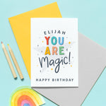 Load image into Gallery viewer, A colourful typographic card with a personalised name and the words &#39;you are magic! Happy birthday&#39;. The card features a large light grey star in the background with a collection of smaller stars around the lettering.
