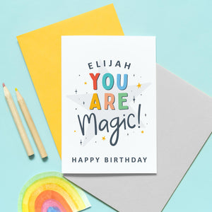 A colourful typographic card with a personalised name and the words 'you are magic! Happy birthday'. The card features a large light grey star in the background with a collection of smaller stars around the lettering.