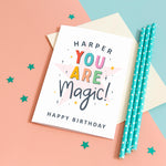 Load image into Gallery viewer, A colourful typographic card with a personalised name and the words &#39;you are magic! Happy birthday&#39;. The card features a large light pink star in the background with a collection of smaller stars around the lettering.
