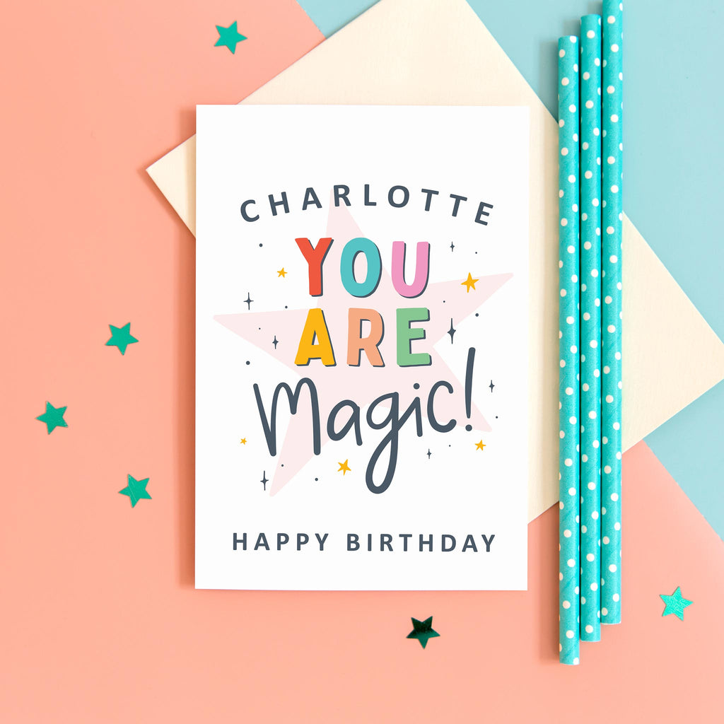 A colourful typographic card with a personalised name and the words 'you are magic! Happy birthday'. The card features a large light pink star in the background with a collection of smaller stars around the lettering.